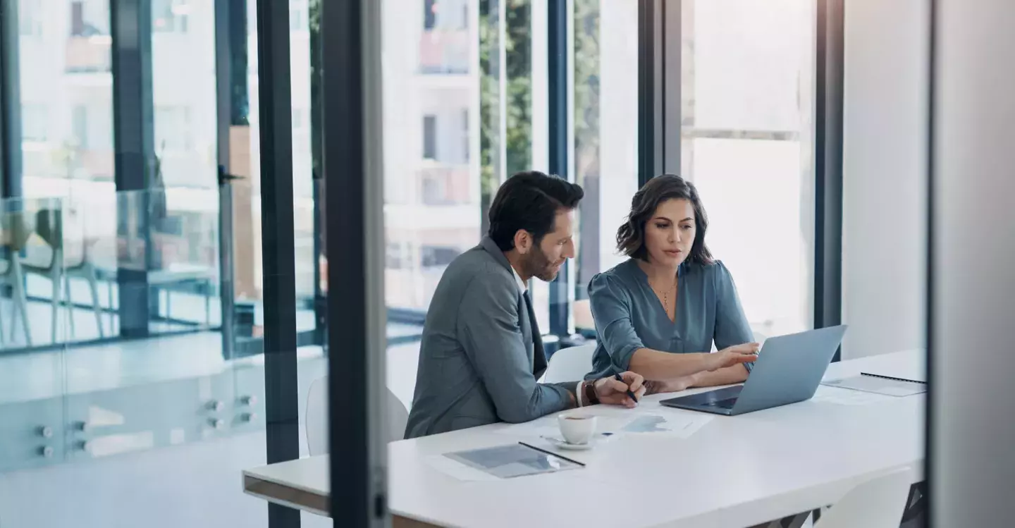 Man and women sitting at a desk and looking at a laptop